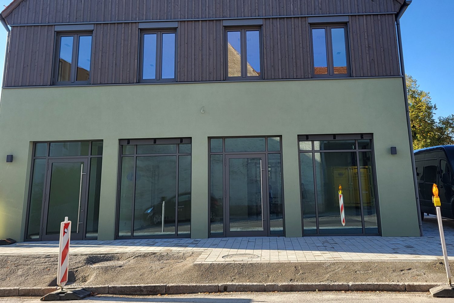 Der Neubau von der Straße aus: grüne Fassade mit vier großen Glasfronten und zwei Eingängen im Erdgeschoss