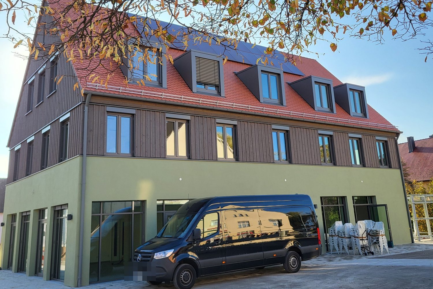 Seitenansicht des Neubaus mit Holzfassade, rotem Ziegeldach und Glasfronten im Erdgeschoss